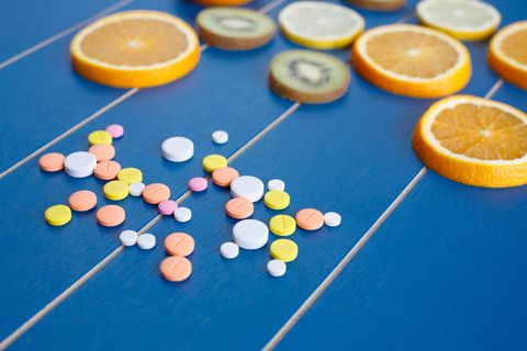 Pills of vitamin C and various citrus fruits sliced on blue wooden board. Healthy foods and medicine concept. Mixed fruits sliced orange, lemon and kiwi. Vitamins from foods or supplements choices