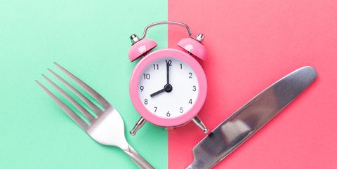 pink alarm clock, fork, knife on colored paper background intermittent fasting concept
