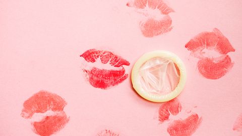 Lipstick kisses on pink background with condom