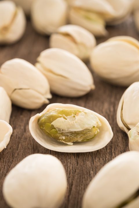 a shelled pistachio and pistachios in shells on a wooden table, a good housekeeping pick for a healthy weight loss food