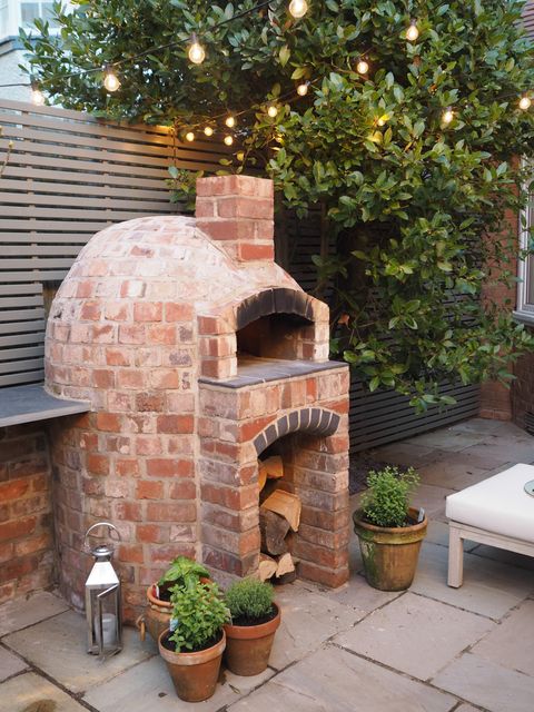 stone pizza oven with with a variety of plants and a large tree in outdoor kitchen ideas
