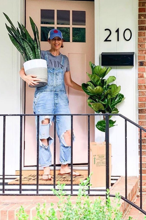 A woman on a porch carrying one plant with one in a box beside her