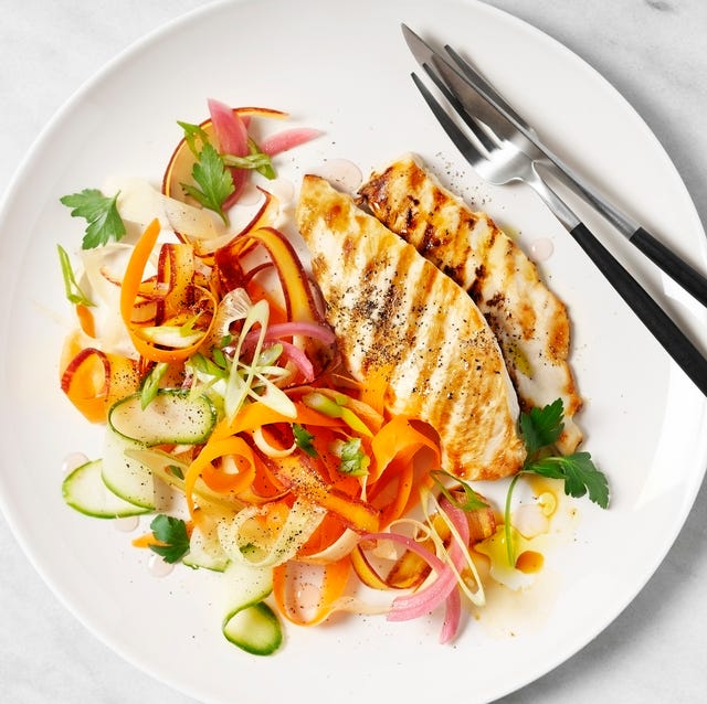 a plate of grilled chicken with carrot salad on white background