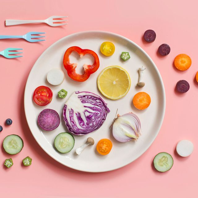 Plato con verduras y frutas sobre fondo rosa.