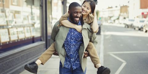 Playful young couple piggybacking on urban street