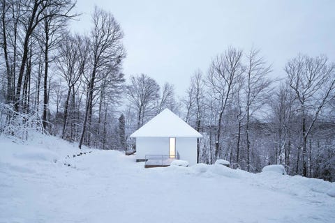 una casa de montaña con cubierta a dos aguas blanca que se camufla con la nieve y los árboles de la montaña