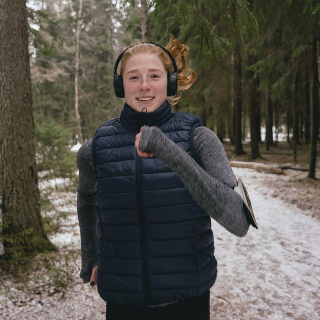 vrouw loopt hard in het bos met een hardloop bodywarmer tijdens de winter