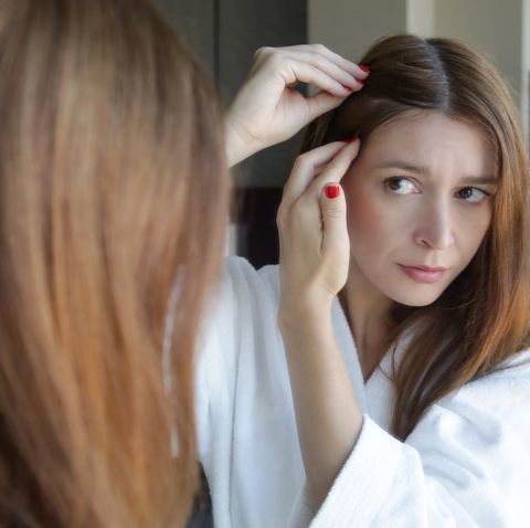 portrait of a beautiful young woman examining her scalp and hair in front of the mirror, hair roots, color, grey hair, hair loss or dry scalp problem