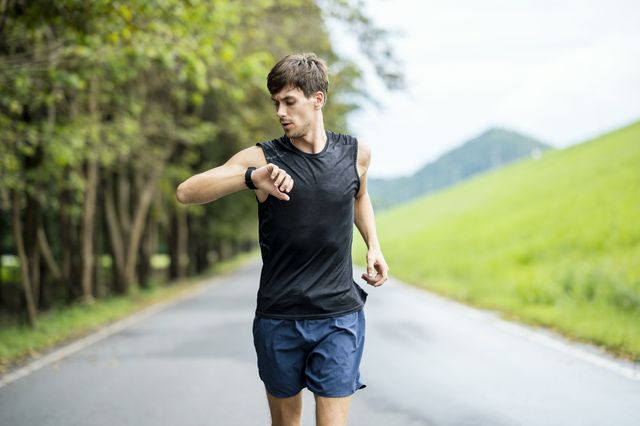 portrait of a caucasian male athlete using wearable run tracking technology while jogging on the street
