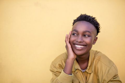 Portrait of a smiling young woman wearing yellow jacket in front of yellow wall