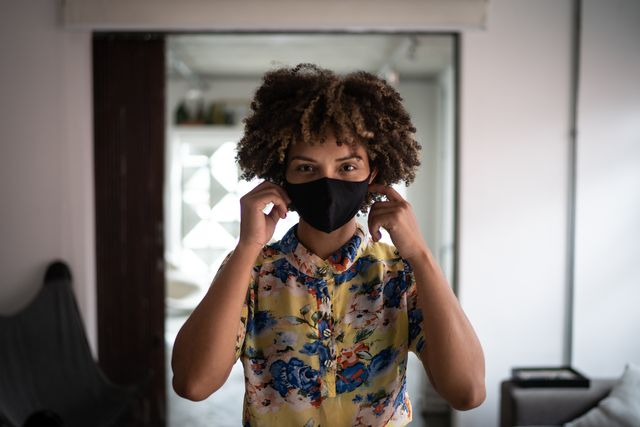 portrait of a young woman putting on protective face mask at home