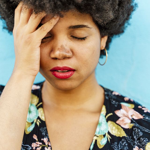 portrait of afro american woman, hand on forehead, blue wall in the background