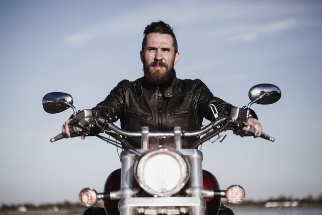 portrait of confident biker sitting on motorcycle against sky