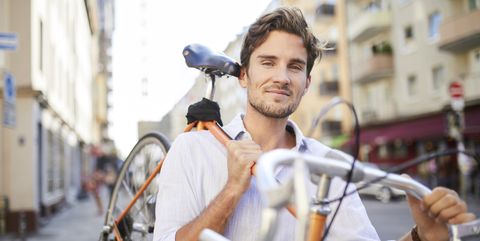 Portrait of content young man carrying his racing cycle on shoulder in the city