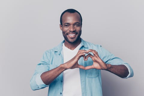 portrait of creative, romantic, positive, cheerful, confident guy making love symbol, heart figure with fingers, looking at camera, isolated on grey background