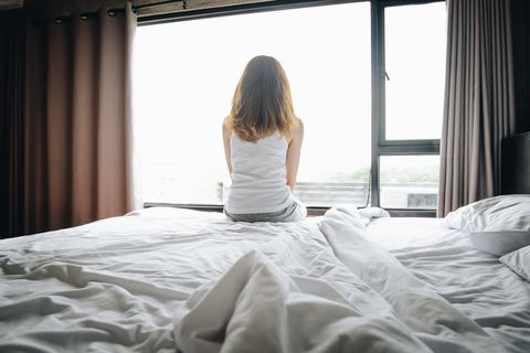 portrait of depressed woman sitting alone on bed, looking to outside the window
