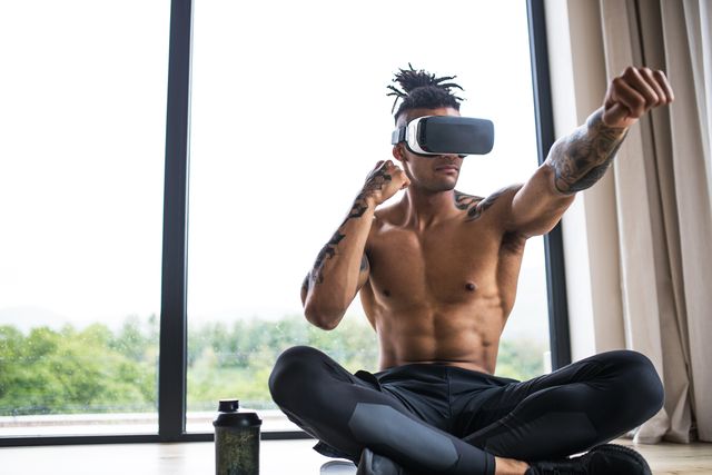 a portrait of fit mixed race man with vr goggles doing exercise at home, in boxing position