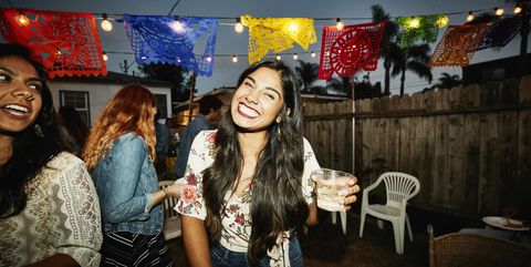 Portrait of laughing woman sharing drinks with friends in backyard on summer evening