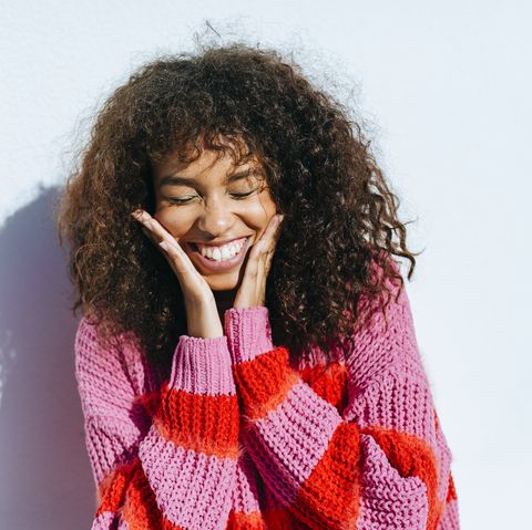 portrait of laughing young woman with curly hair against white wall