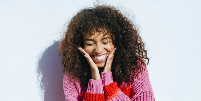 portrait of laughing young woman with curly hair against white wall