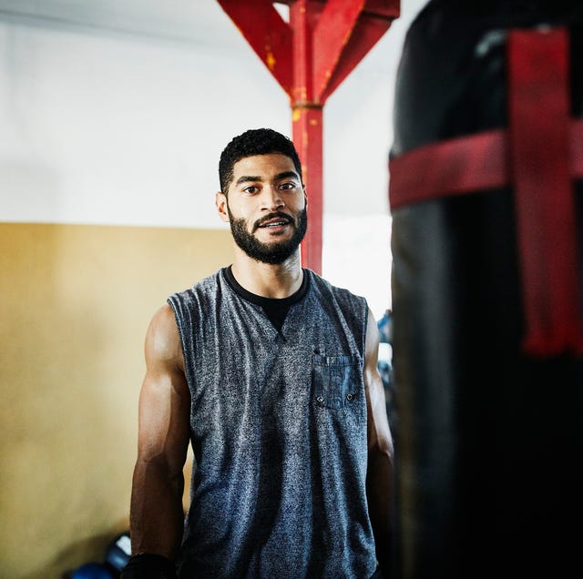 Portrait of male boxer standing by heavy bag in boxing gym