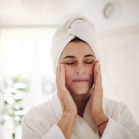 portrait of mature woman in a bathroom at home applying moisturizer