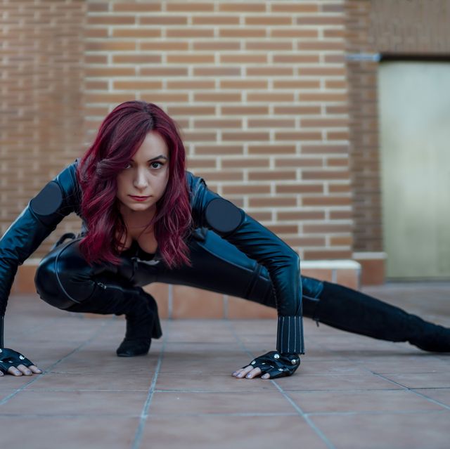 portrait of redheaded woman wearing black leather catsuit crouching on rooftop