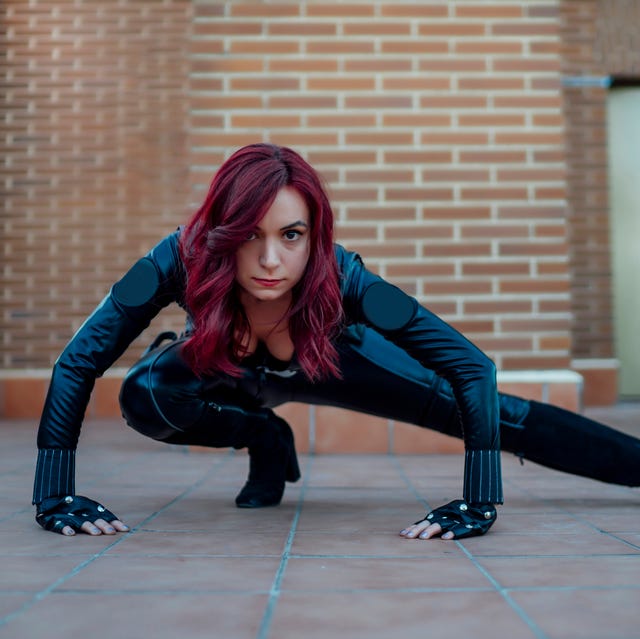 portrait of redheaded woman wearing black leather catsuit crouching on rooftop