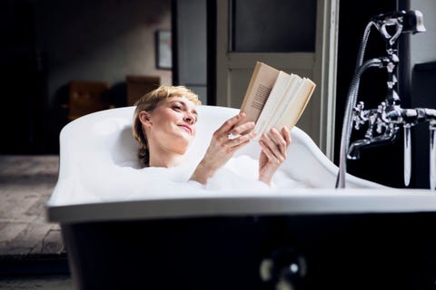 Portrait of relaxed woman taking bubble bath in a loft reading a book