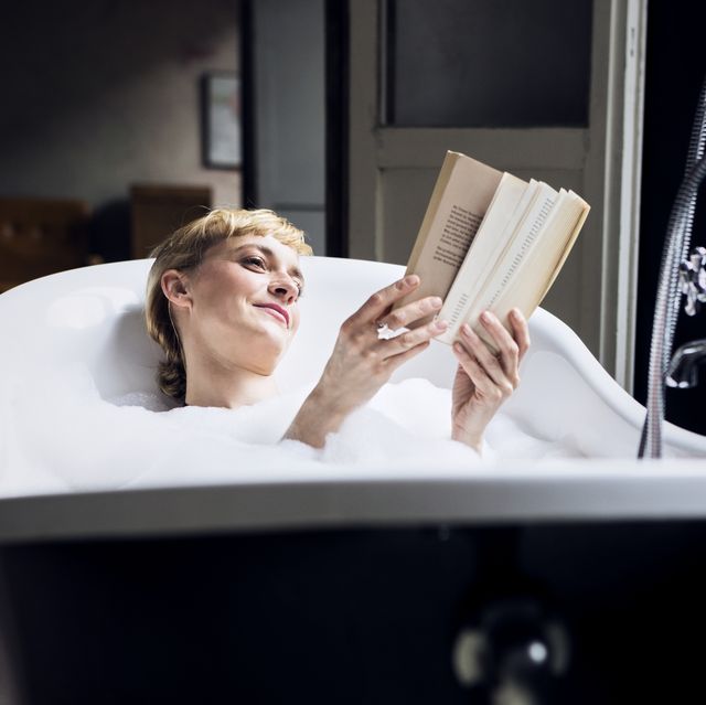 portrait of relaxed woman taking bubble bath in a loft reading a book