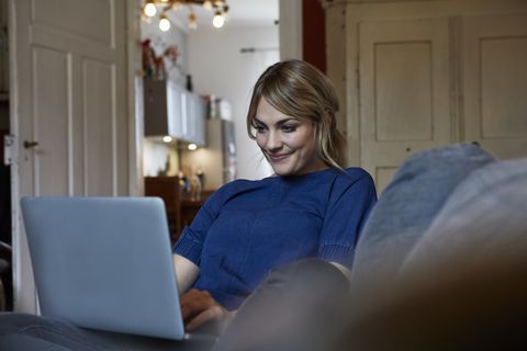 Portrait of smiling woman using laptop on couch at home