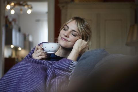 portrait of smiling woman with cup of tea relaxing on couch at home