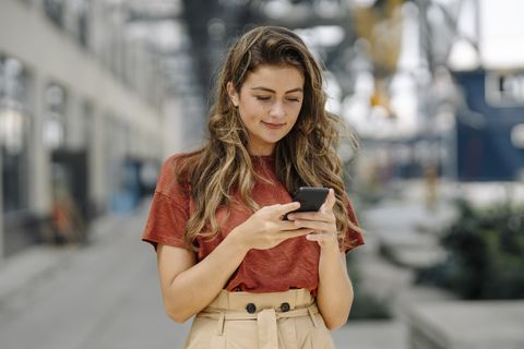 portrait of smiling young brunette woman using smartphone, looking down