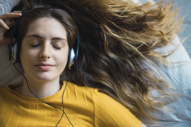 portrait of smiling young woman lying on bed listening music with headphones