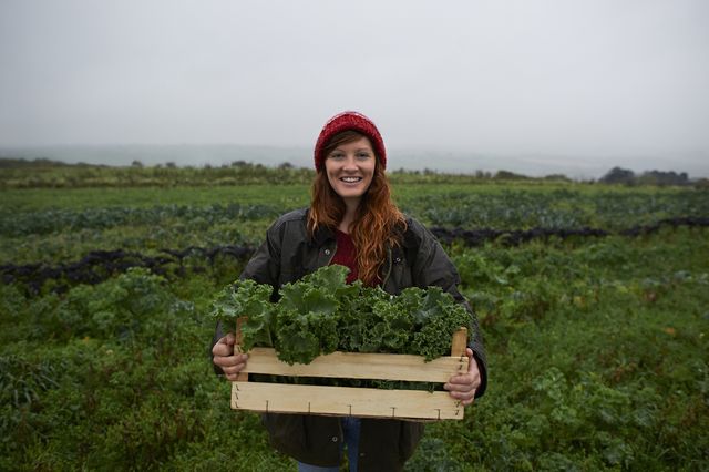 portrait of woman holding box of kale on farm