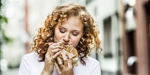 portrait of young woman eating bagel outdoors