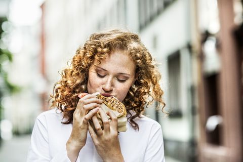 Mujer comiendo un bagel por la calle.