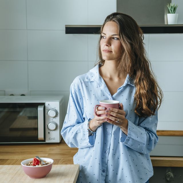 portrait of young woman wearing pyjama in kitchen at home holding cup of coffee