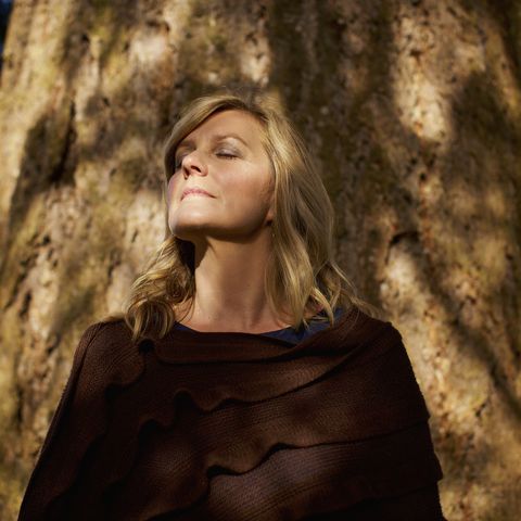 portrait serene woman with eyes closed standing at sunny tree trunk