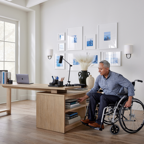 man in wheelchair reaches for books on the open shelving attached to the side of the l shaped pottery barn pacific desk