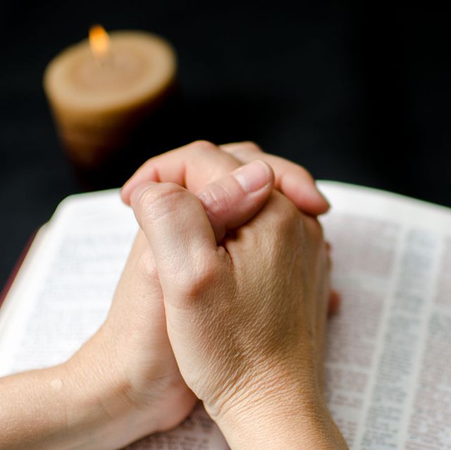 prayers for the sick clasped hands on top of an open bible with a lit candle