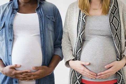 two pregnant women standing next to each other holding bellies