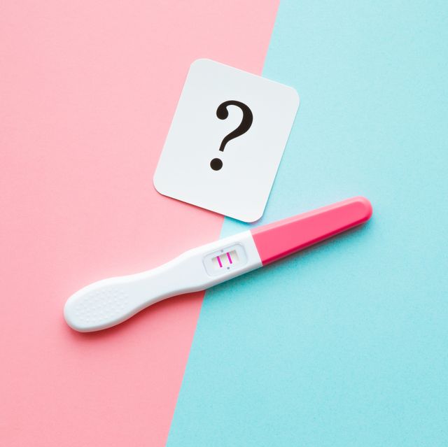 pregnancy test with two stripes and white card of black question mark pastel blue and pink background positive result guessing unborn baby gender closeup