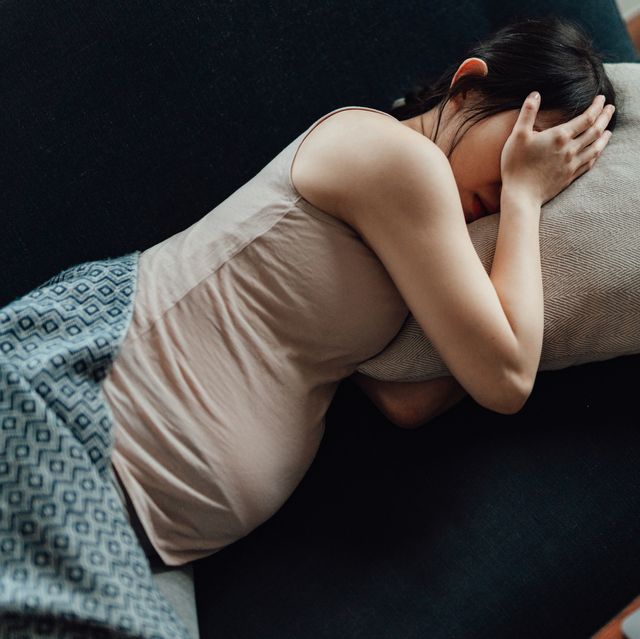 pregnant woman covering her eyes with hands while laying on sofa