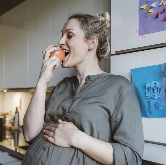 una embarazada se toma una manzana en su cocina