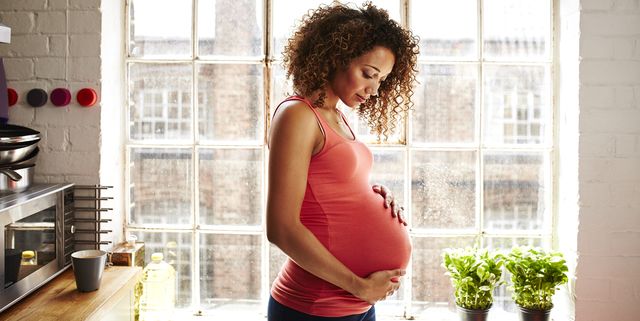 a pregnant woman holds her bump in kitchen window