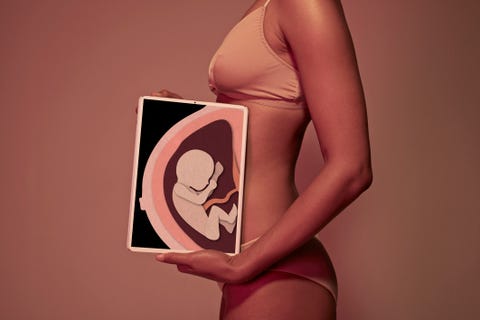 Pregnant young woman holding tablet in front of belly to display baby