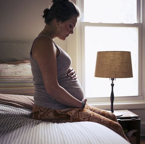 pregnant young woman sitting on bed at home