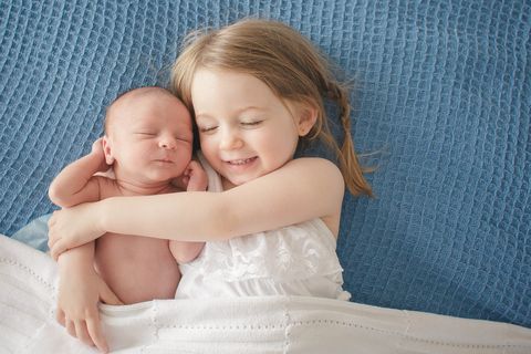 preschool girl hugs newborn baby brother
