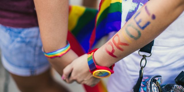 two people holding hands with rainbow bracelets and pride written on arm